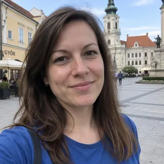 Portré Boglárka Váradiról, egy harmincas éveiben járó nőről, barna hajjal, kék ingben