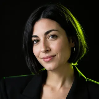 Ritratto di Arianna Ruffato, una donna sulla trentina con capelli castani raccolti, maglione verde scuro