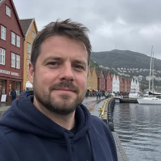 Portrett av Lukas Haugland, en mann i slutten av trettiårene med kort skjegg og en mørkeblå hettegenser